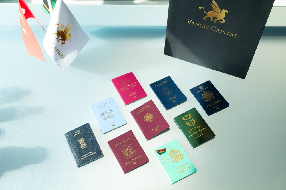 Nine passports in various colors are arranged on a light surface near a Vancis Capital bag and small flags, suggesting an international context related to Golden Visa programs